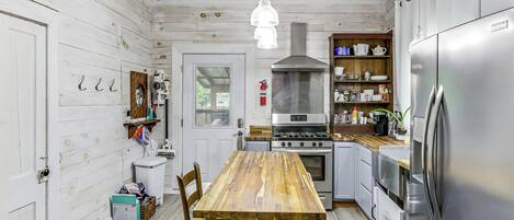 Et køkken med et træbord, rustfrie hårde hvidevarer og en hængende lampeskærm.
