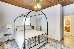 Un lit à baldaquin avec un couvre-lit blanc, une petite table de chevet avec une lampe et un ventilateur de plafond.