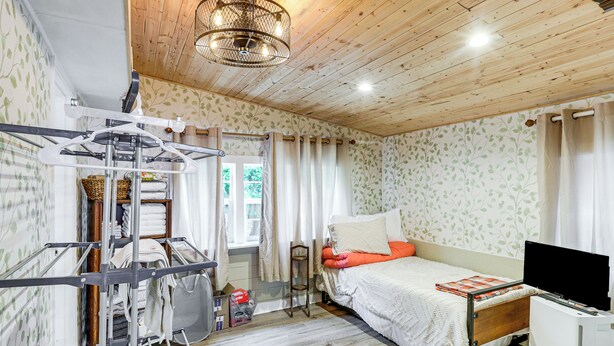 Un dormitorio con techo de madera, una cama con ropa blanca, un televisor y un tendedero.