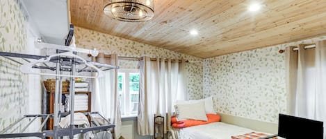 Un dormitorio con techo de madera, una cama con ropa blanca, un televisor y un tendedero.
