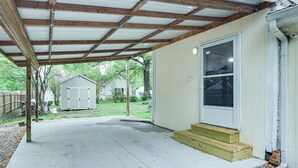A covered patio area with a wooden beam ceiling, a concrete floor, and a set of wooden steps leading to a white door. - Cozy Carterville Home: 3 Mi to Crab Orchard Lake! (Carterville)