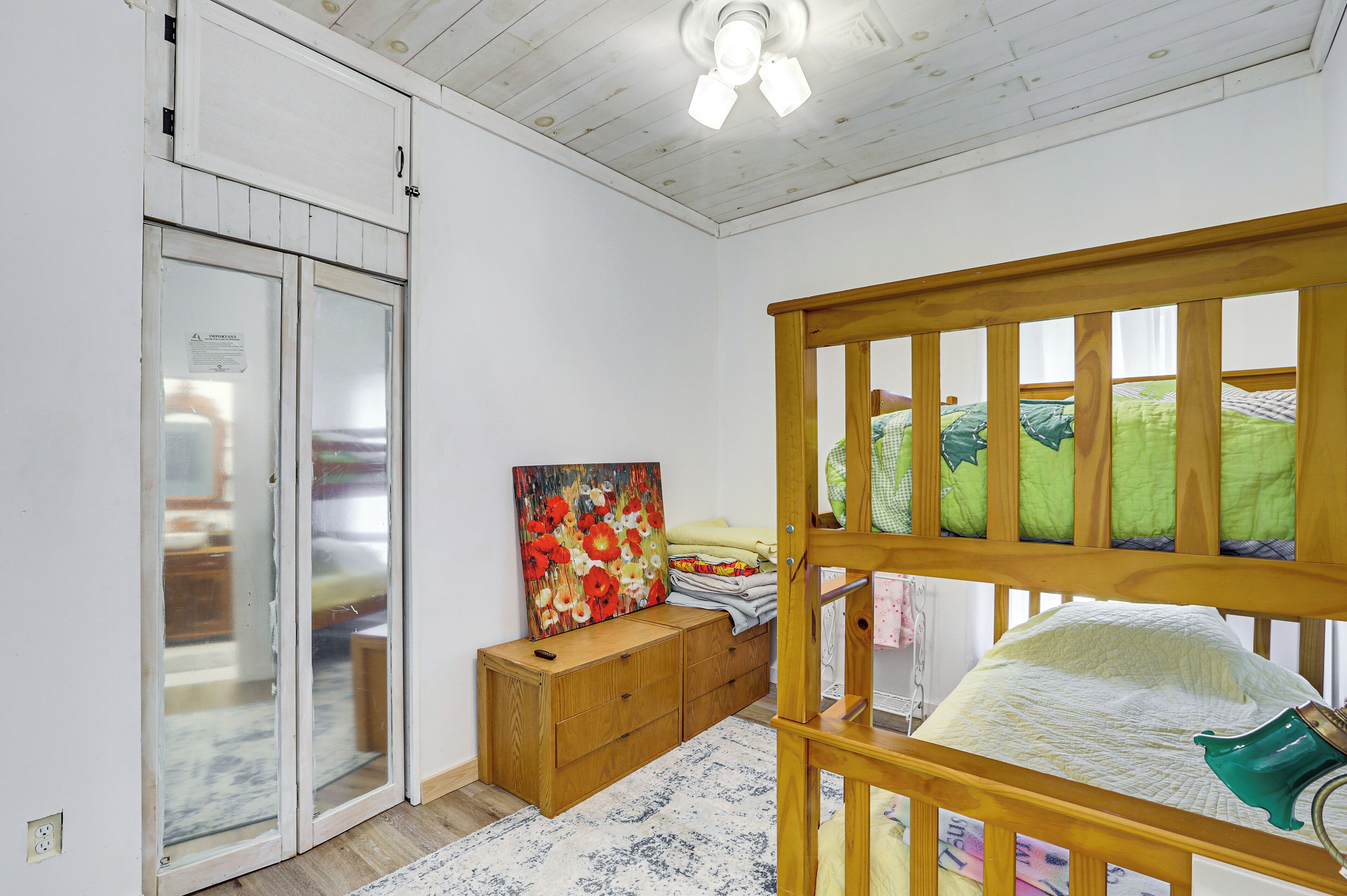 A bedroom with a wooden bunk bed, a wooden cabinet, a painting, and a ceiling fan.