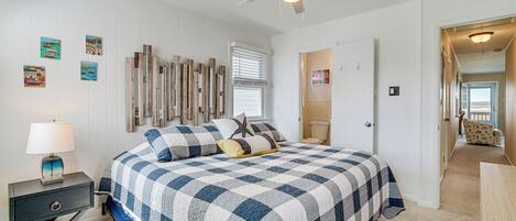 A bedroom with a large bed, a ceiling fan, a nightstand, and a wall with wooden panels and artwork.
