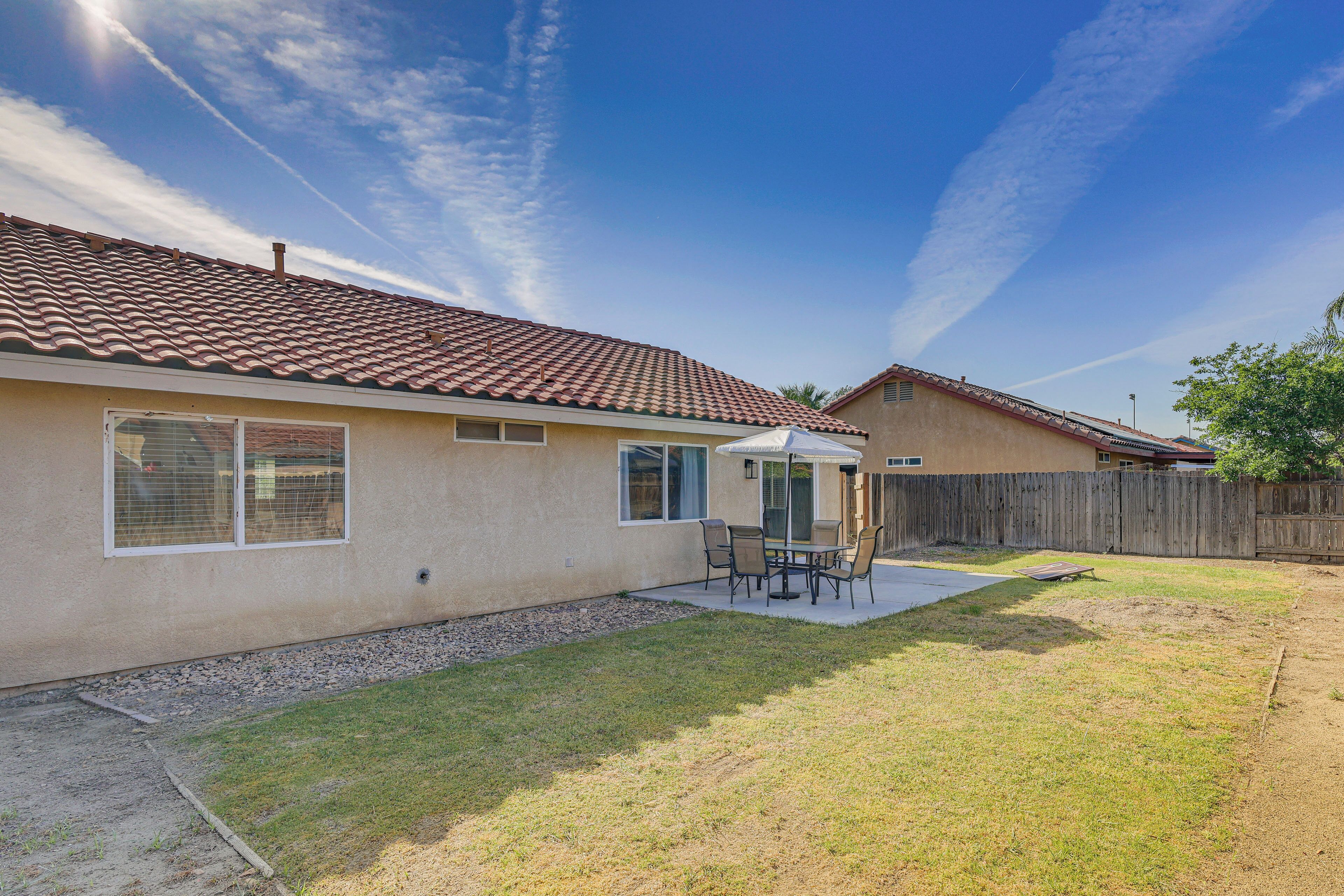 Un jardin à l’arrière d’une maison, avec une terrasse, une clôture en bois et un ciel dégagé.