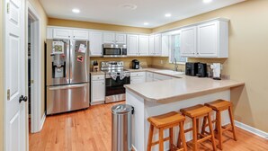 A modern kitchen with white cabinets, stainless steel appliances, and a wooden bar stool area. - Cozy Hermitage Home w/ Deck: 11 Mi to Nashville! (Hermitage)
