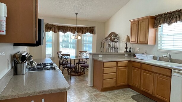A kitchen with a dining area, featuring a gas stove, wooden cabinets, and a window with blinds. - Private Pool Paradise close to Lake Sumter Landing Market Square! (The Villages)