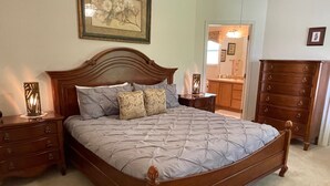 A bedroom with a large bed, wooden headboard, two nightstands, a dresser, and a framed picture on the wall. - Private Pool Paradise close to Lake Sumter Landing Market Square! (The Villages)