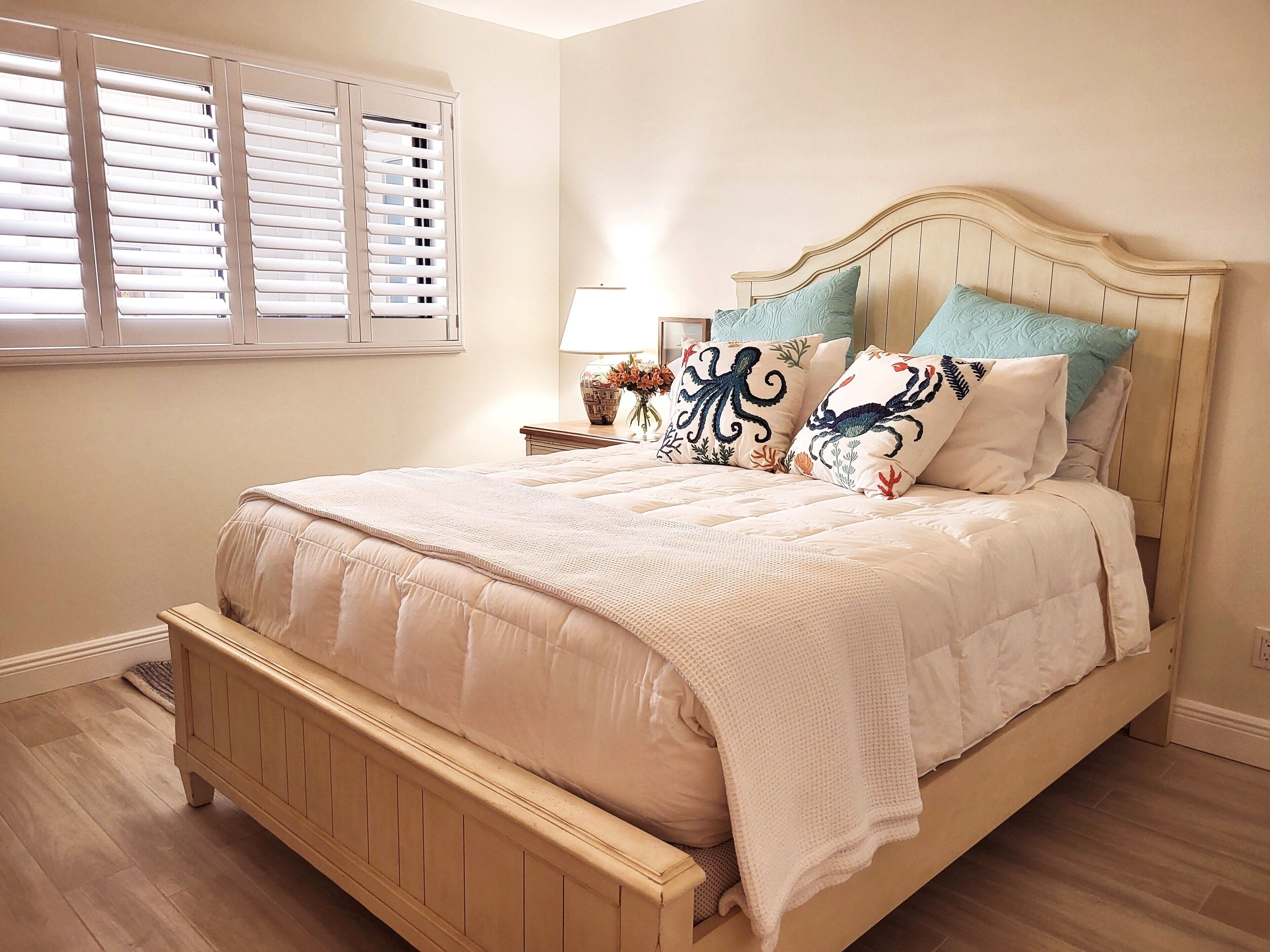 A bedroom with a wooden bed frame, a beige quilted bedspread, and decorative pillows with a sea-themed design.
