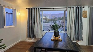 A room with a large window, curtains, a wooden table, and a potted plant. - Stargaze Grand Canyon (Meadview)