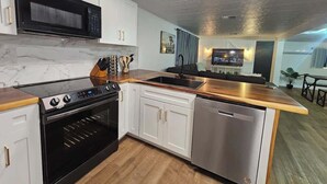 A modern kitchen with a built-in oven, microwave, and dishwasher, wooden countertops, and white cabinetry. - Stargaze Grand Canyon (Meadview)