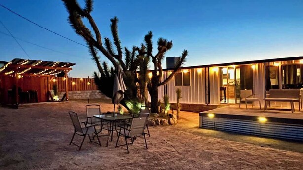A desert-style outdoor area with a dining table and chairs, a cactus, and a modern building with large windows. - Stargaze Grand Canyon (Meadview)