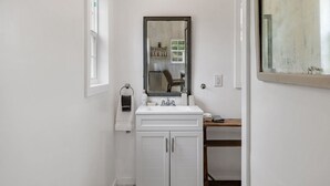A narrow bathroom with a white sink, a mirror above it, and a wooden shelf below.