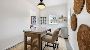 A compact kitchen with a wooden table and chairs, a hanging light fixture, and woven wall decorations.