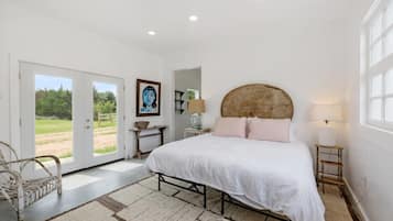Une chambre à coucher avec un lit, une table de chevet, une lampe, une chaise et une vue sur l’extérieur, visible à travers une porte.