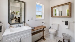 A bathroom with a white sink, a wooden vanity, a toilet, a large mirror, and a window.