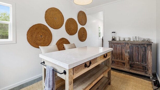 A kitchen with a white marble countertop, wooden cabinets, and woven wall decorations.