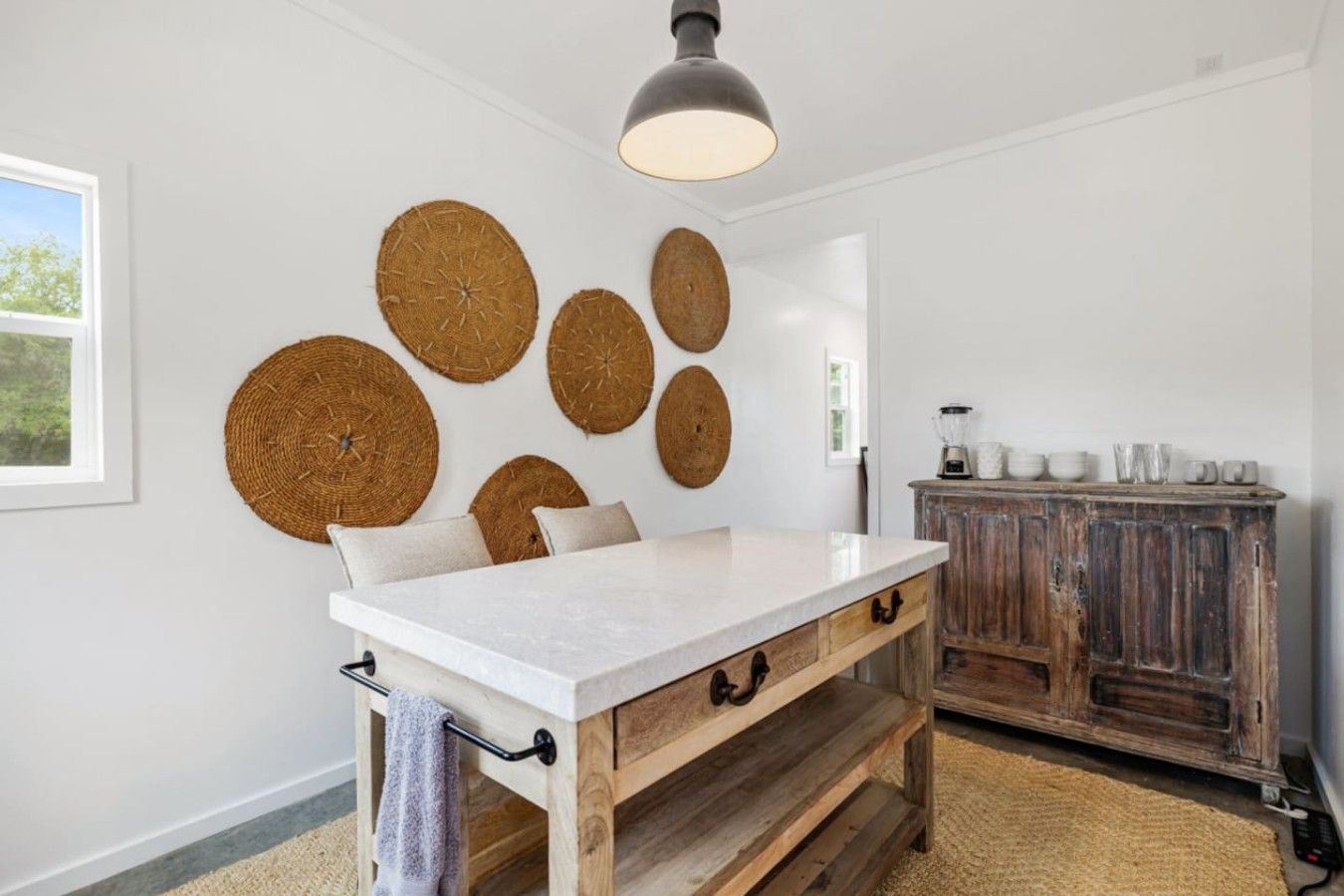 Een keuken met een marmeren aanrechtblad, houten keukenkastjes en wanddecoraties van geweven materiaal.