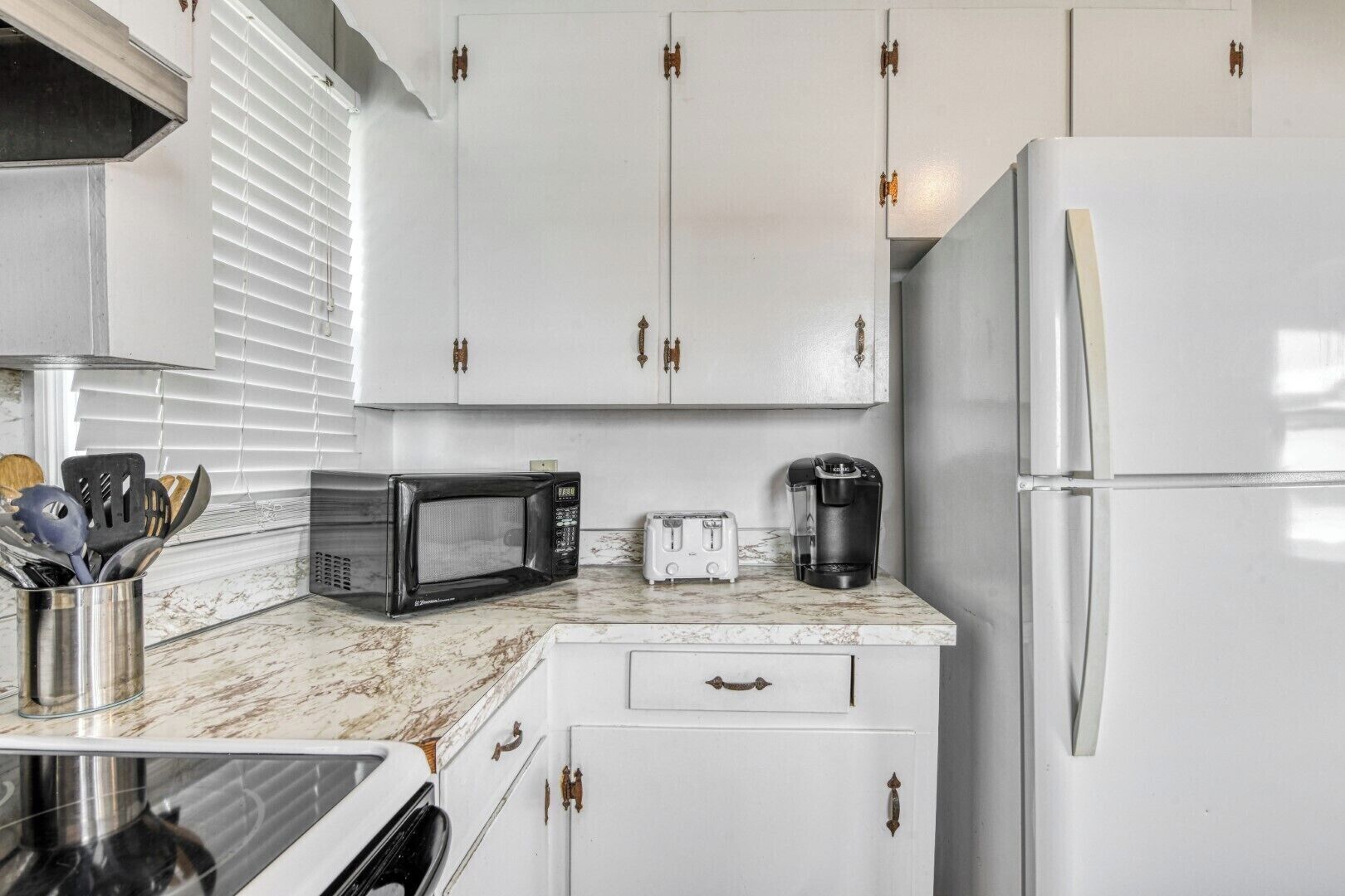 A kitchen with white cabinets, a microwave, a toaster, and a coffee maker on a marble countertop.