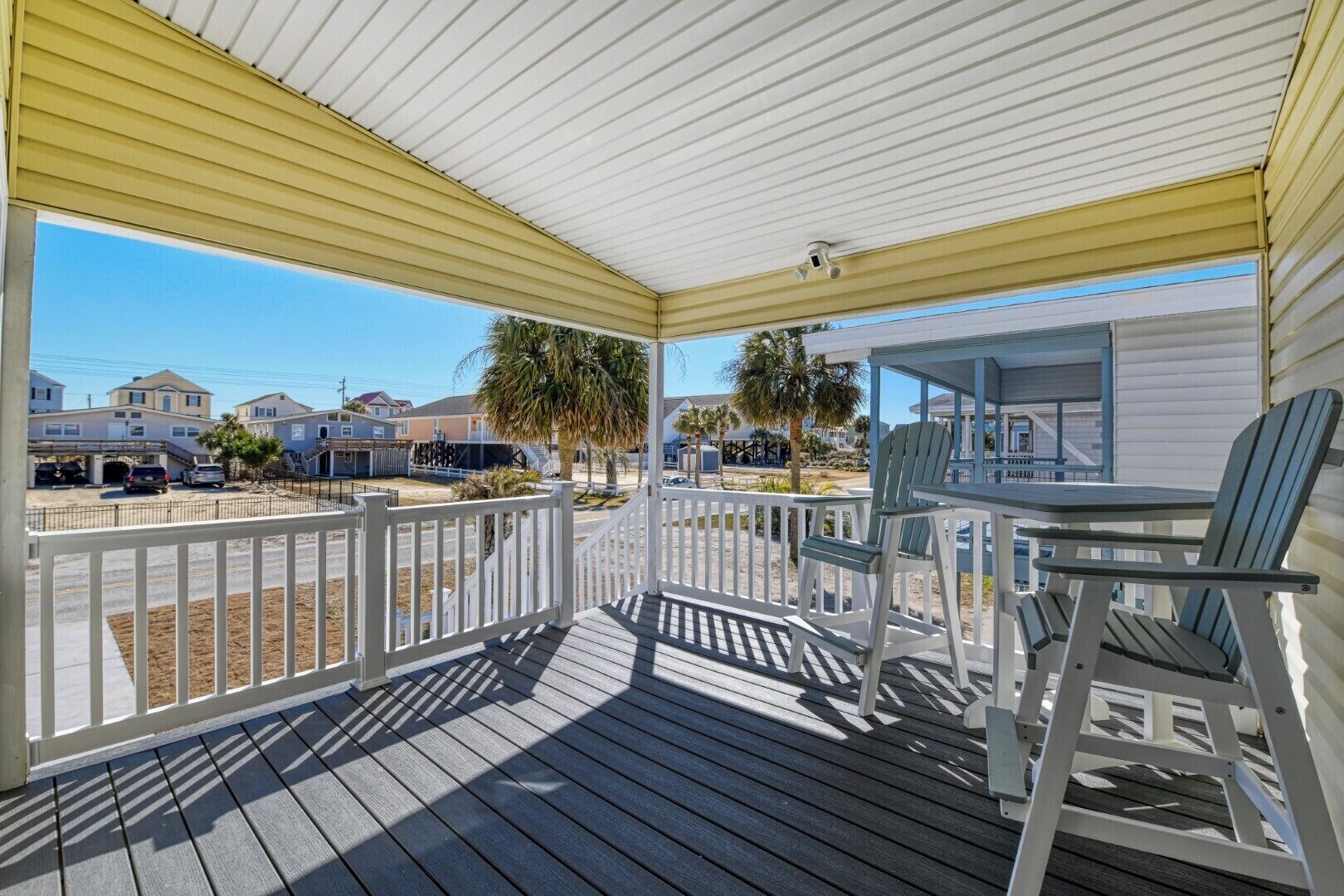 A covered porch with a view of a residential area, including houses and a street.