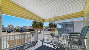 A covered porch with a view of a residential area, including houses and a street.