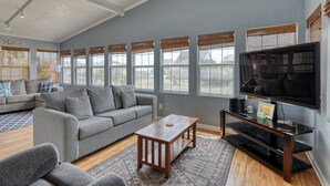A spacious living room with a grey sofa, a wooden coffee table, and a flat-screen TV.