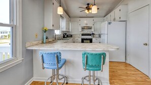 A kitchen with a marble countertop, two bar stools, a ceiling fan, and a view of the outside.