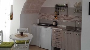 Une cuisine de taille réduite, dotée d’un plan de travail blanc, d’un évier et d’une cuisinière. On y trouve également un coin repas avec une table et des chaises.