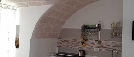 A compact kitchen with a white countertop, a sink, and a stove. There is a dining area with a table and chairs.