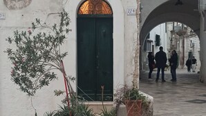 Une ruelle étroite pavée de pierres, avec une porte verte, des plantes en pot et un pont piétonnier.