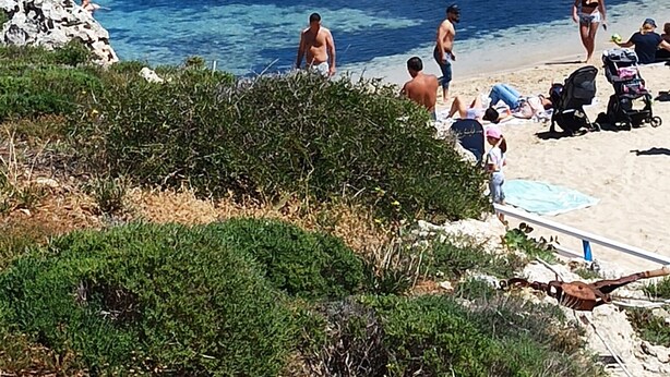 Une plage de galets avec une eau claire, des gens qui se prélassent au soleil et quelques enfants qui jouent.