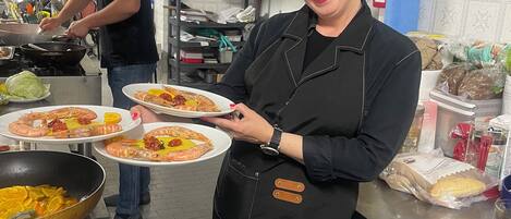 Une cuisine équipée d’appareils électroménagers en acier inoxydable, une personne tenant des assiettes de nourriture et une autre personne en train de cuisiner.