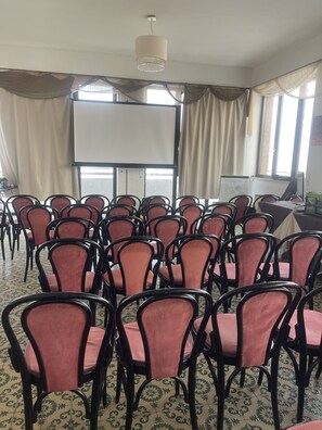 A conference room with rows of chairs, a projector screen, and a chandelier. - LEONE (Rimini)