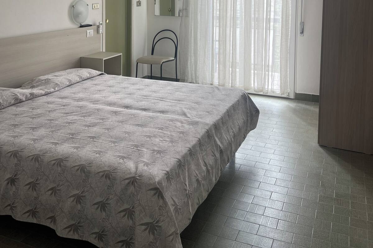 A bedroom with two beds, a chair, a wardrobe, a mirror, and a window with curtains.