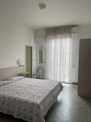 A bedroom with two beds, a chair, a wardrobe, a mirror, and a window with curtains. - LEONE (Rimini)