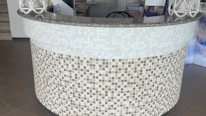 Un comptoir d  ’accueil orné de motifs en mosaïque, un bureau avec un ordinateur et une porte visible au fond.