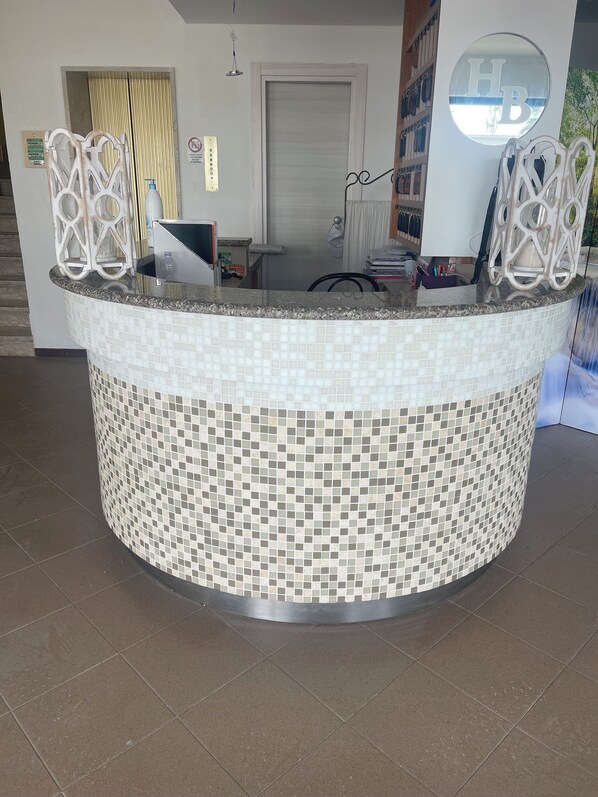 Un comptoir d’accueil orné de motifs en mosaïque, un bureau avec un ordinateur et une porte visible au fond.