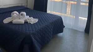 Une chambre d’hôtel avec un lit, des toilettes fixées au mur, une fenêtre avec des rideaux et une vue sur la mer.