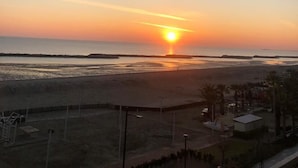 Une vue sur le coucher de soleil depuis un balcon donnant sur une plage, avec un ciel dégagé.