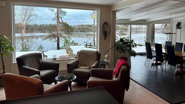 A spacious living room with large windows overlooking a lake, furnished with leather chairs and a coffee table. - House with fantastic view and direct access to the lake and boat. (Skåne län)