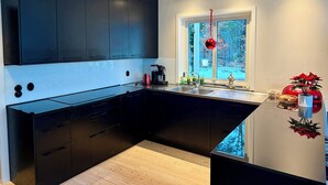 A modern kitchen with dark cabinetry, a wooden countertop, and a window with a view of trees. - House with fantastic view and direct access to the lake and boat. (Skåne län)