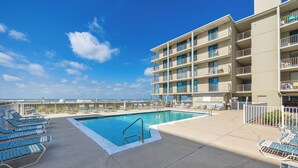 A pool area with lounge chairs and a building with multiple balconies.