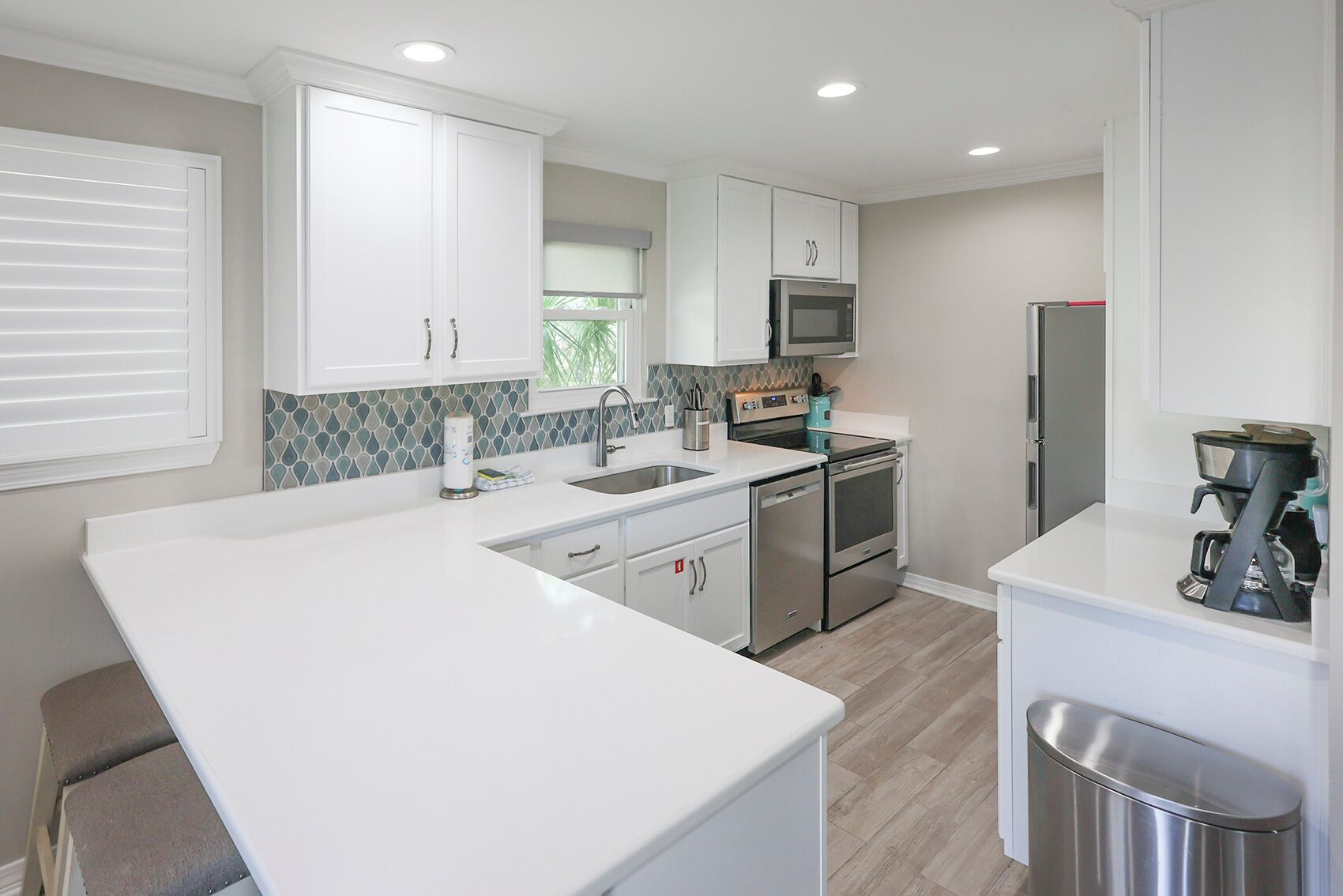 A modern kitchen with white cabinetry, a large island, stainless steel appliances, and a window with blinds.