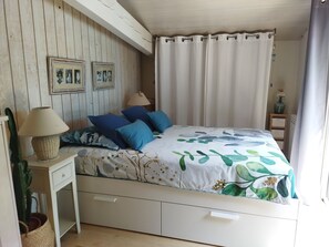 Une chambre à coucher avec un lit, des oreillers, une lampe, une petite table et un cactus.