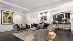 Ein modernes Wohnzimmer mit dunklem Holzboden, einem großen abstrakten Gemälde und einer Küchenzeile mit Barhocker.