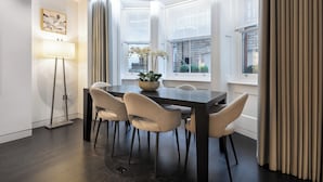 Ein moderner Essbereich mit einem dunklen Holztisch, beigen Stühlen, einer Stehlampe und einer Vase mit weißen Blumen.