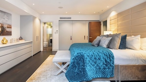 Ein modernes Schlafzimmer mit einem großen Bett, einem Nachttisch, einer Bank und einem Kleiderschrank.