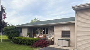 A house with a porch, outdoor seating, and a stone accent wall. - Spacious In-Town Family Home, Walk to Beach & Downtown, Quiet Retreat (Charlevoix)