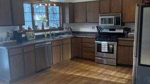 A modern kitchen with wooden cabinets, a stainless steel stove, and a microwave. - Spacious In-Town Family Home, Walk to Beach & Downtown, Quiet Retreat (Charlevoix)