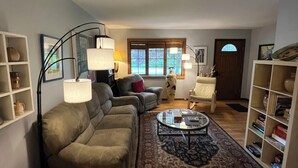A living room with a sofa, armchairs, a coffee table, and a bookshelf. - Spacious In-Town Family Home, Walk to Beach & Downtown, Quiet Retreat (Charlevoix)