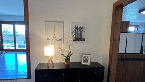 A room with a black console table, a lamp, a potted plant, and two framed pictures of Paris and New York City. - Spacious In-Town Family Home, Walk to Beach & Downtown, Quiet Retreat (Charlevoix)